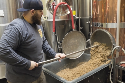Big Alice Brewing's head brewer rakes spent grains from the mash tank for spent grain flour, Queens, New York.
